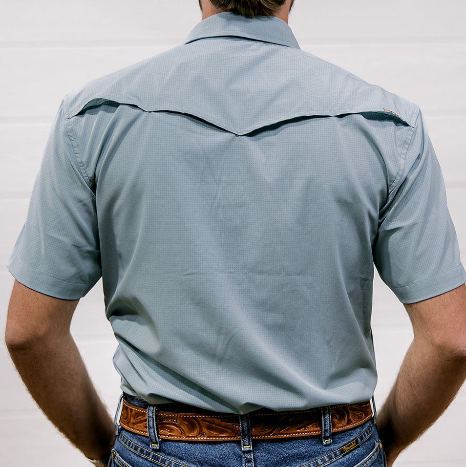 A man wearing a light blue short-sleeve rangevent shirt and jeans with a white background showing the back 