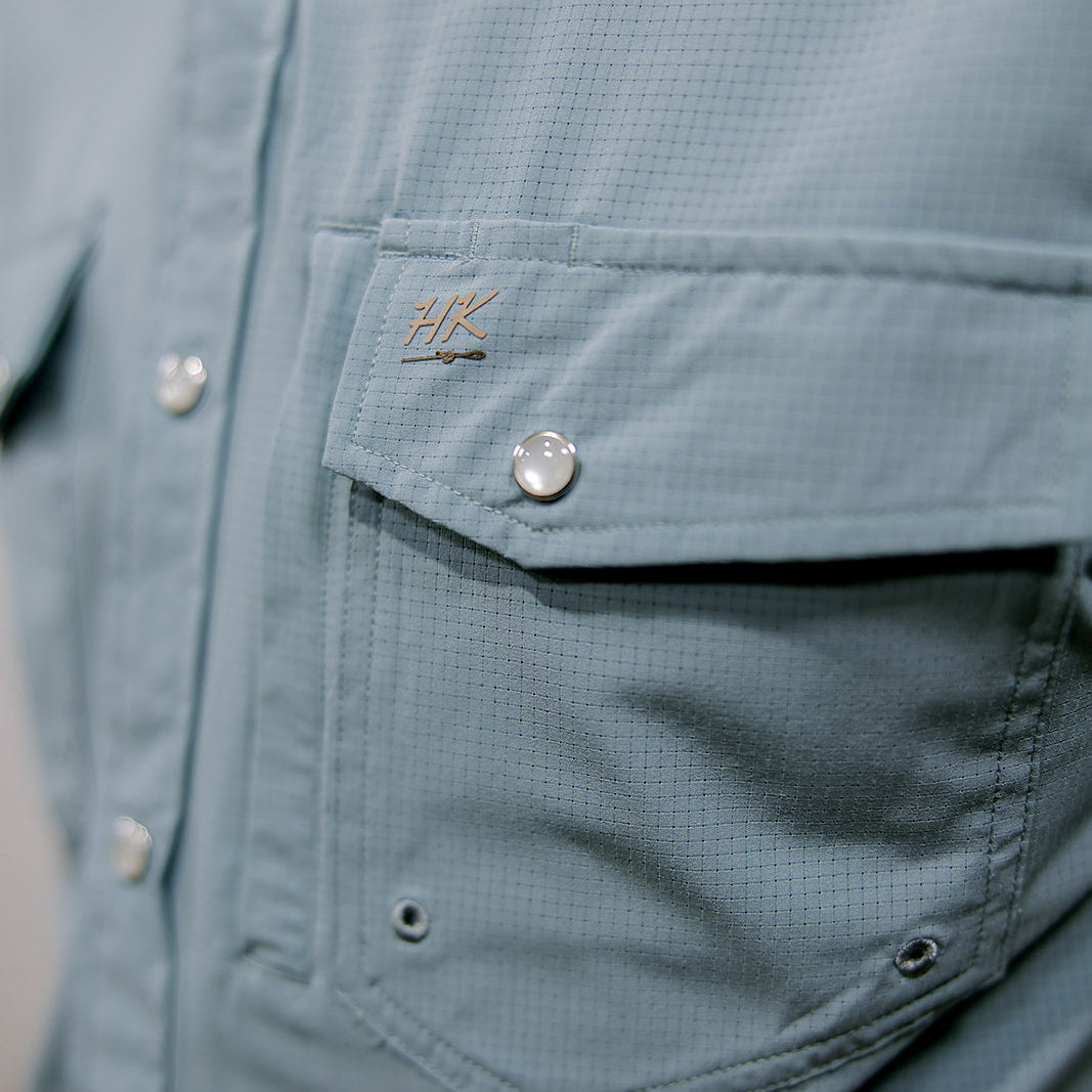 Close-up of a light blue shirt with a brand logo on the chest pocket.