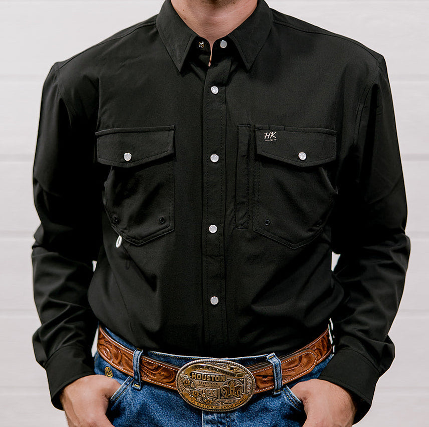 Man wearing a black shirt and blue jeans with a brown belt and large buckle against a white background. Front Facing.
