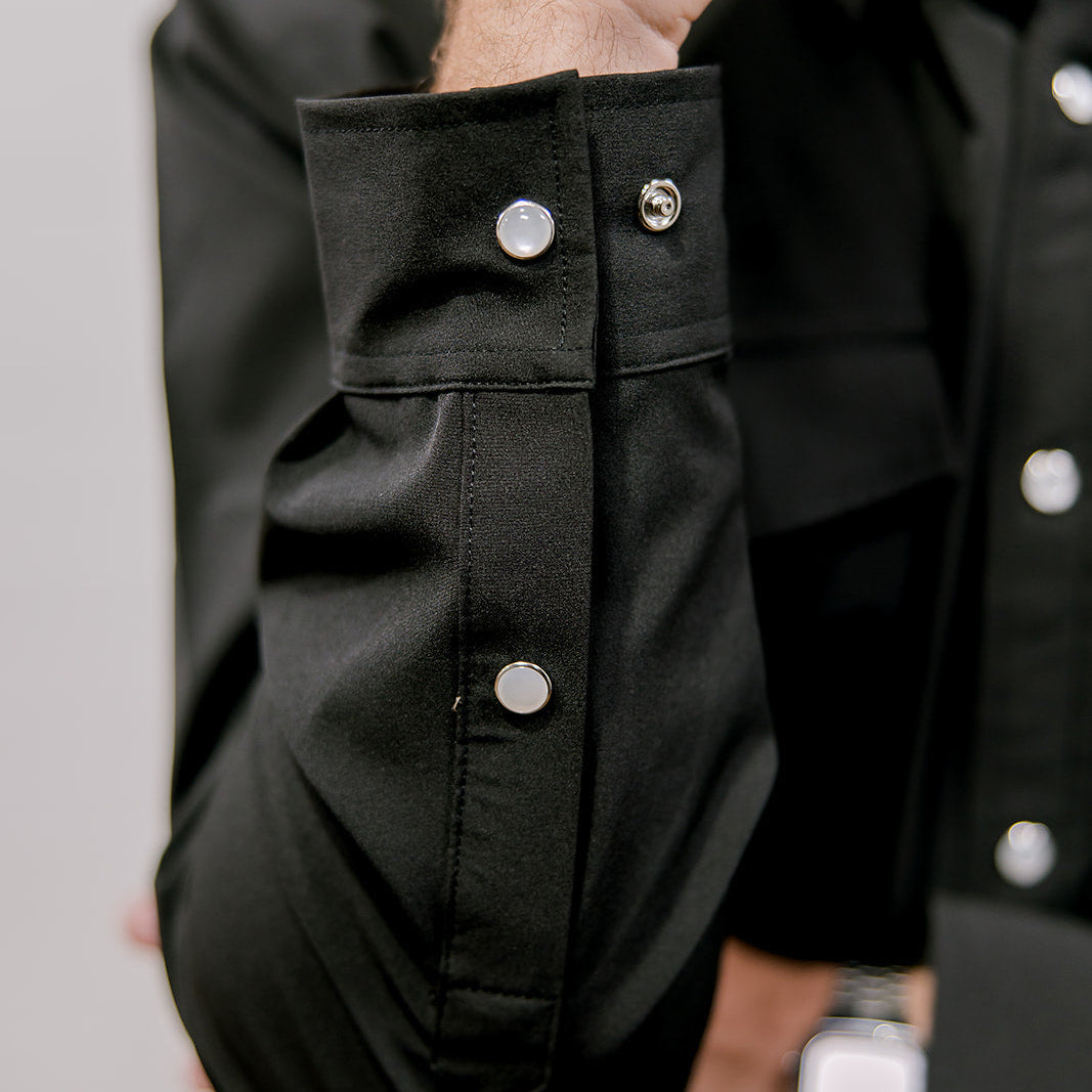 Close-up of a black shirt with white buttons on a plain background. 