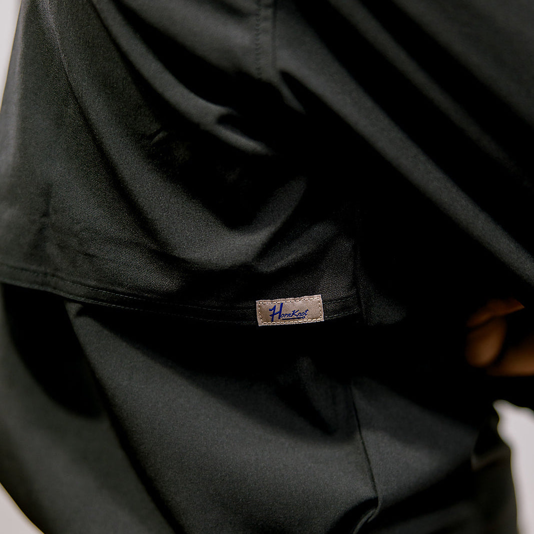 Black Shirt  with a visible brand label worn by a person, with blue jeans and a brown belt. Side Facing