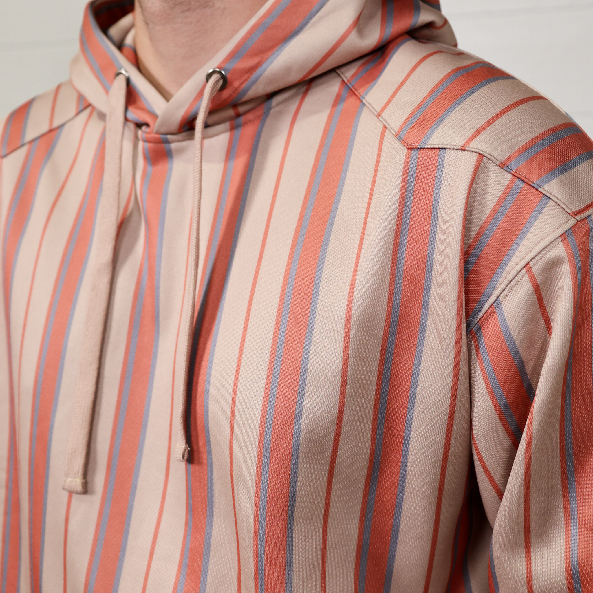 Close-up of a person wearing a striped hoodie with red and beige horizontal stripes.