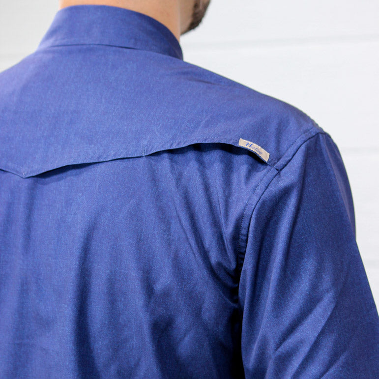 Close-up back view of a person wearing a blue long-sleeve button-up shirt, showing the shoulder and upper back against a light background.