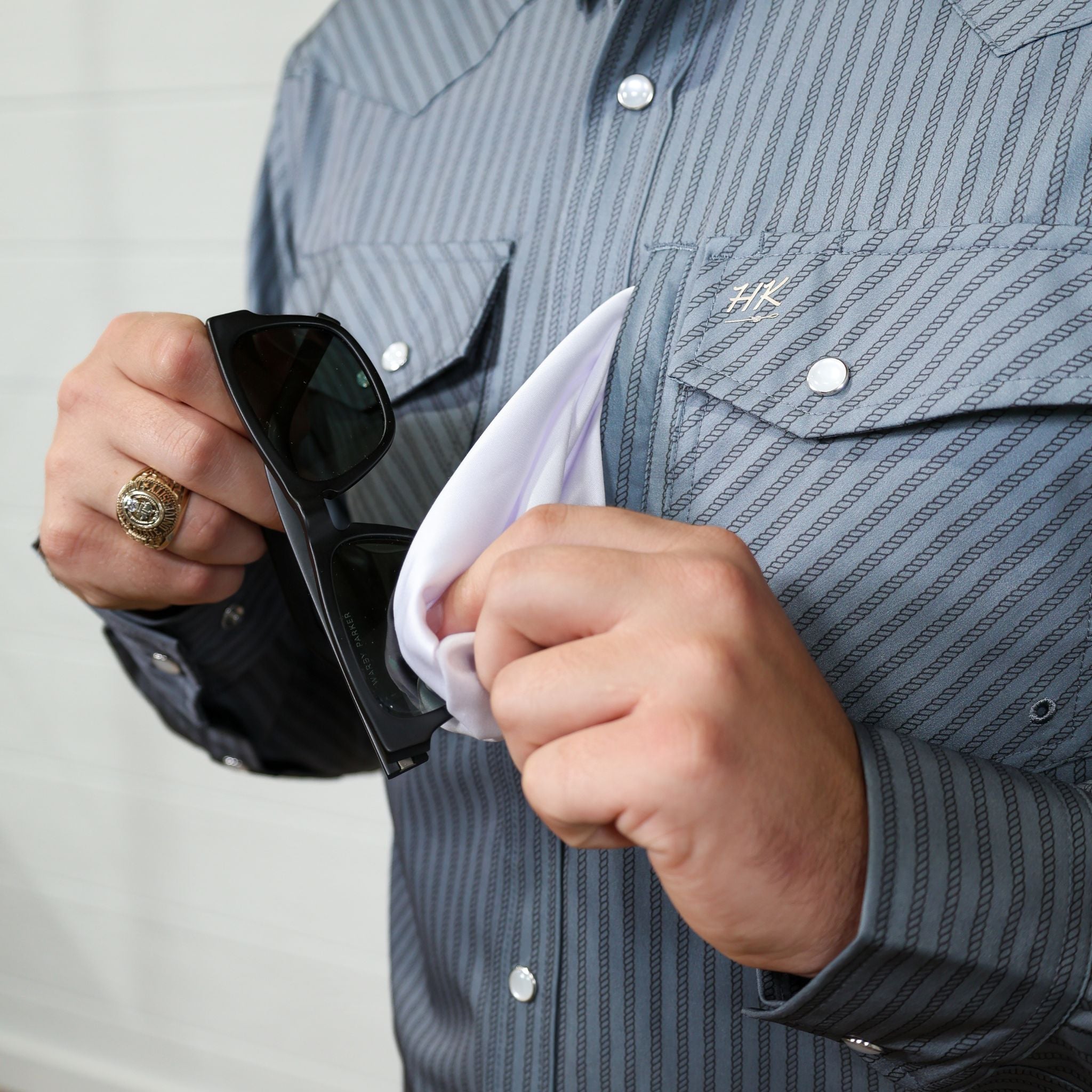 Person wearing a grey striped shirt with a brand logo, holding sunglasses and a white lens cleaner. 