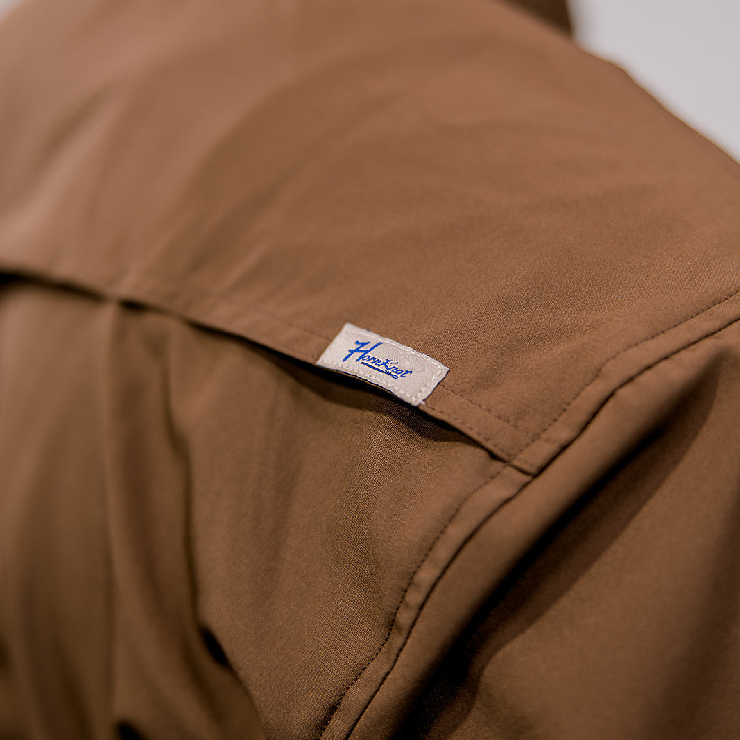 Close-up of a brown shirt with a visible brand label on a plain background