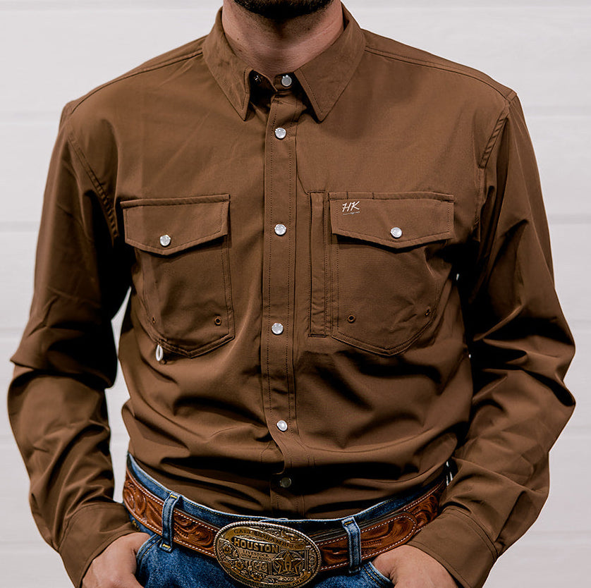 Man wearing a brown shirt and blue jeans with a belt and large buckle against a white background. Front Facing