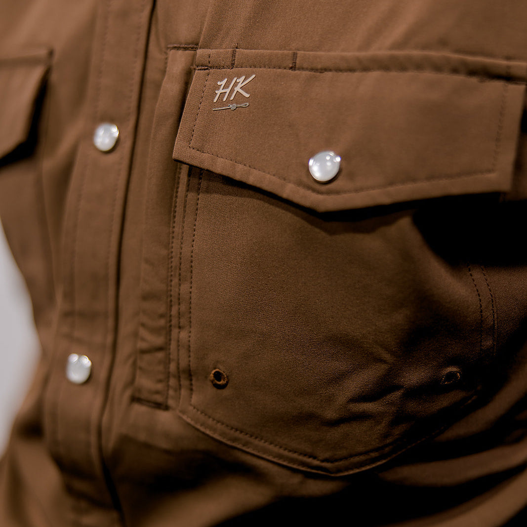 Close-up of a brown shirt with a brand logo on the chest pocket.