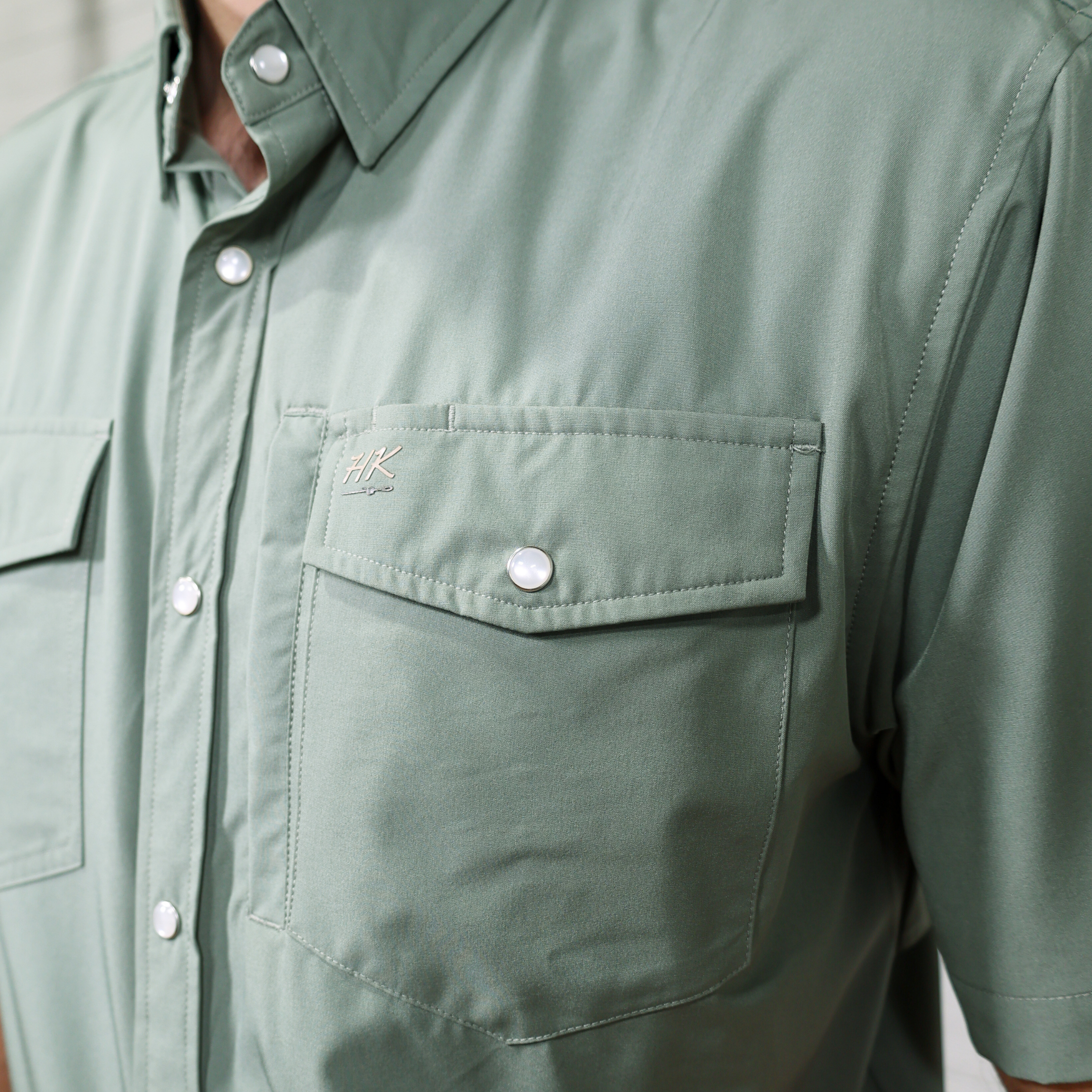 Close-up of a green shirt with a pocket and button details showing brand 