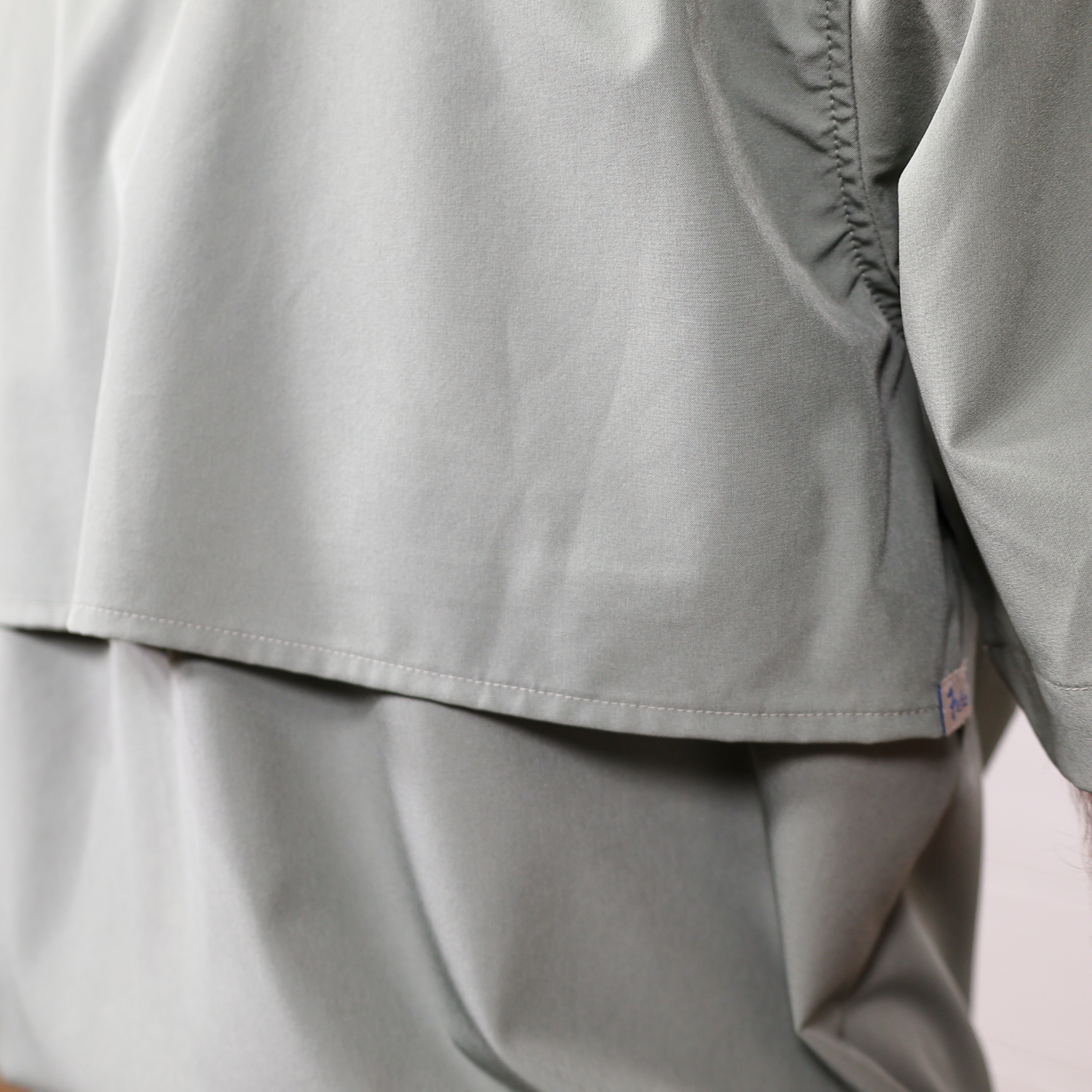 Close-up of a green shirt with a brand logo on a light pink background