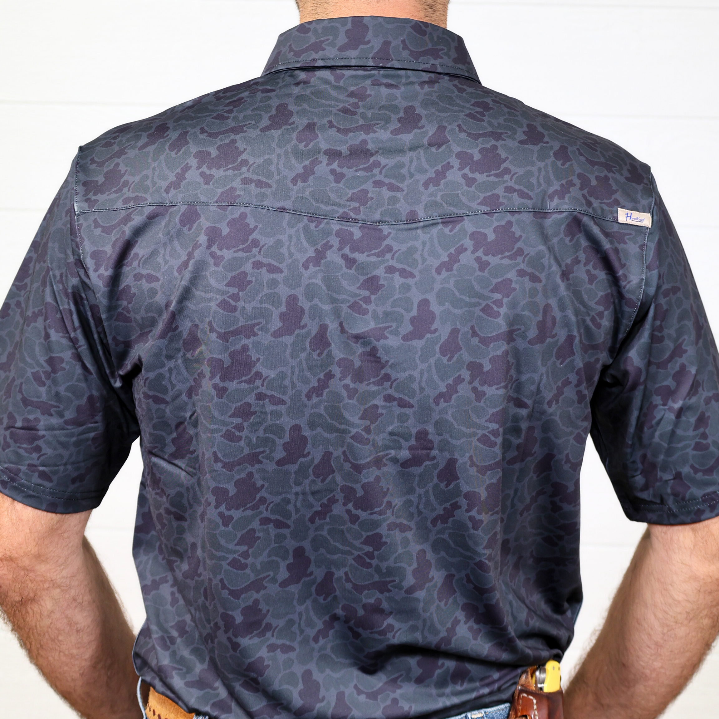 Person wearing a dark camo patterned polo on a plain white background showing the back