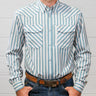 A man wearing a light blue and white vertically striped western long-sleeve shirt, paired with blue jeans and a brown leather belt, standing against a white wood-paneled wall.