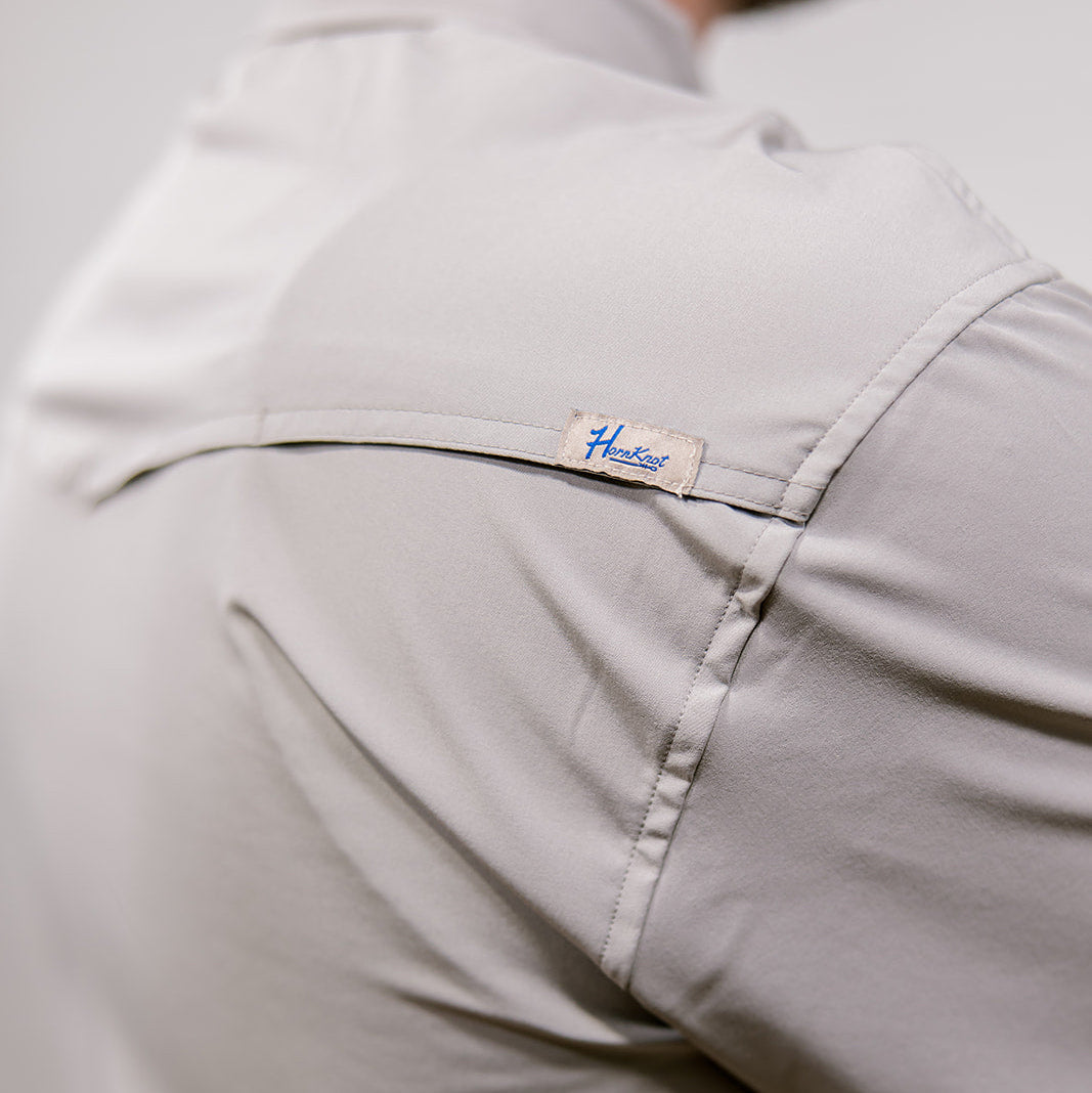 Close-up of a light gray shirt with a brand label on a plain background. Back Facing