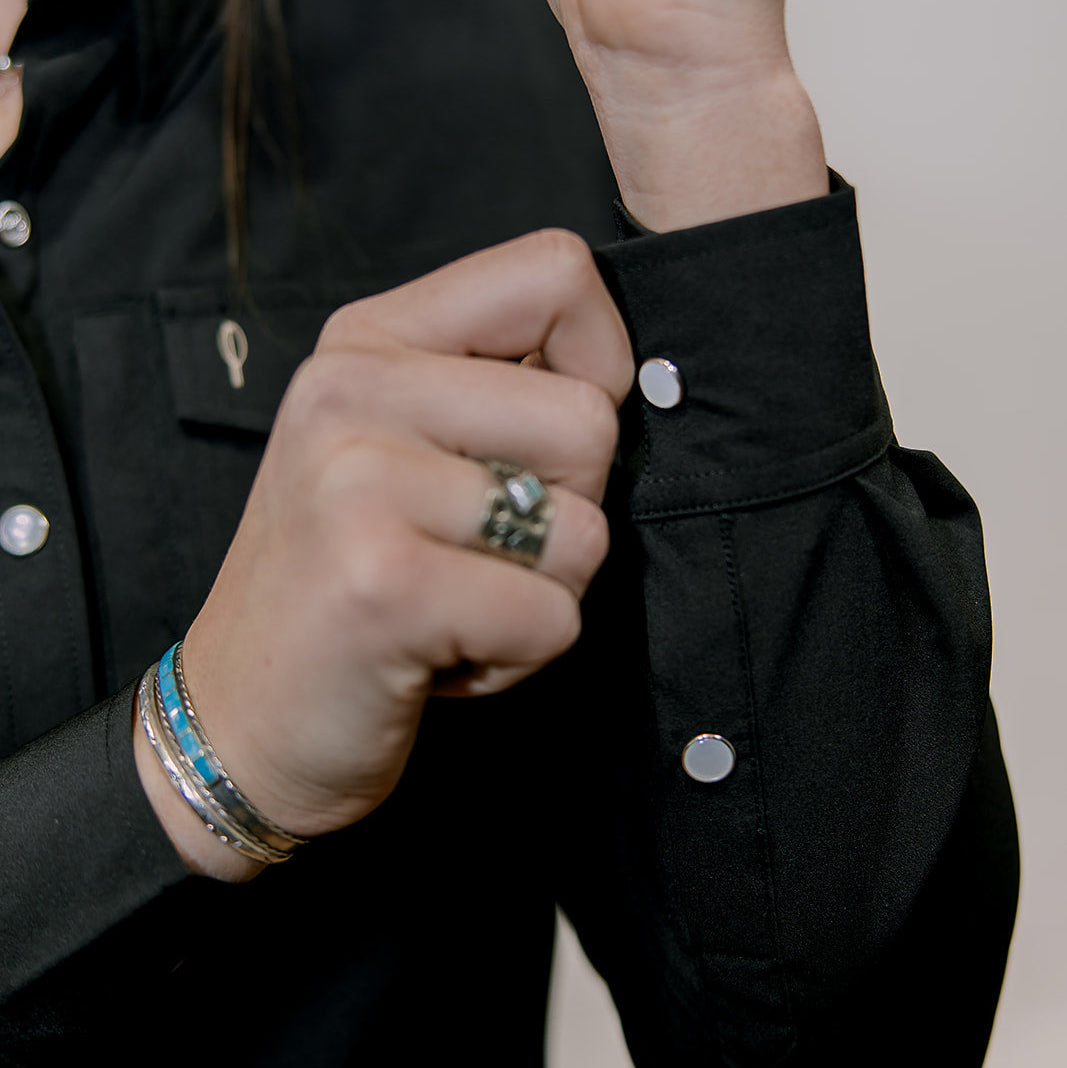 Person buttoning a black shirt with a neutral background