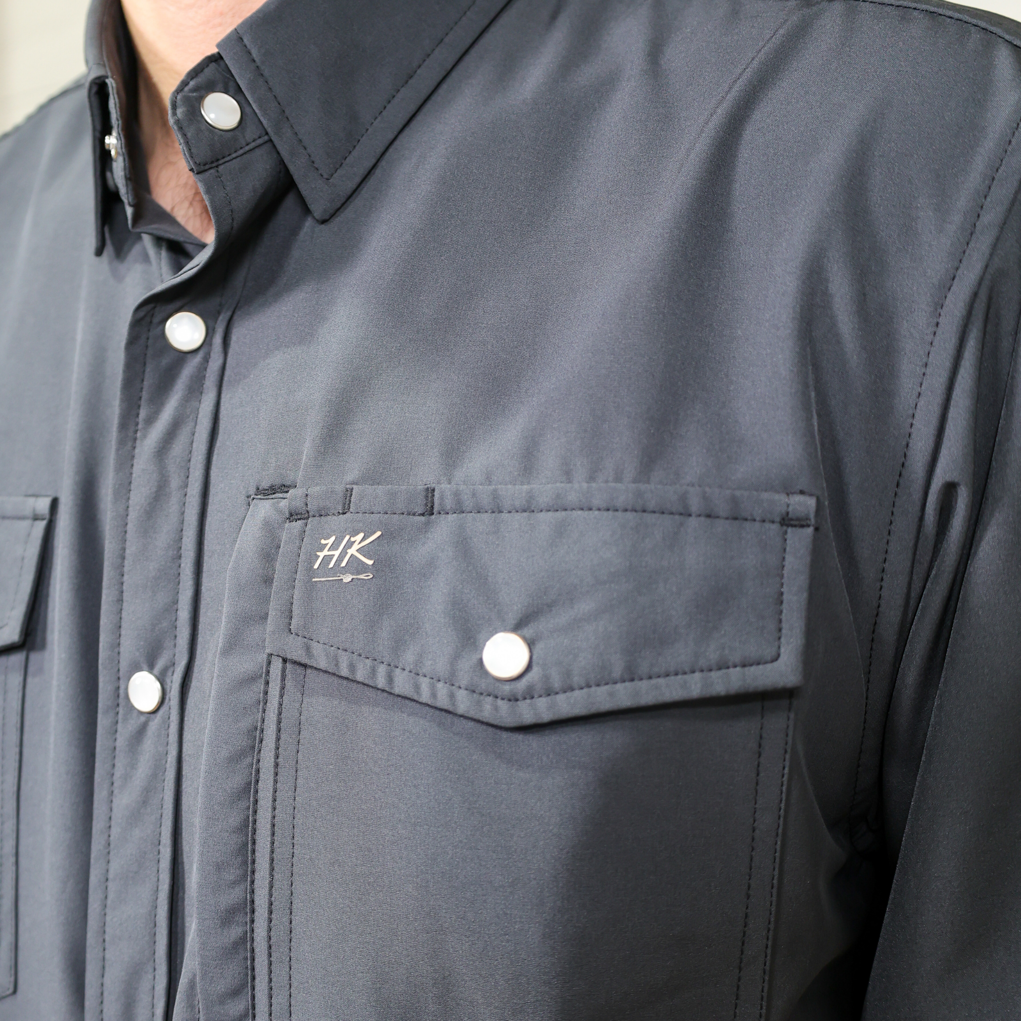 Close-up of a charcoal shirt with a logo on the chest pocket.
