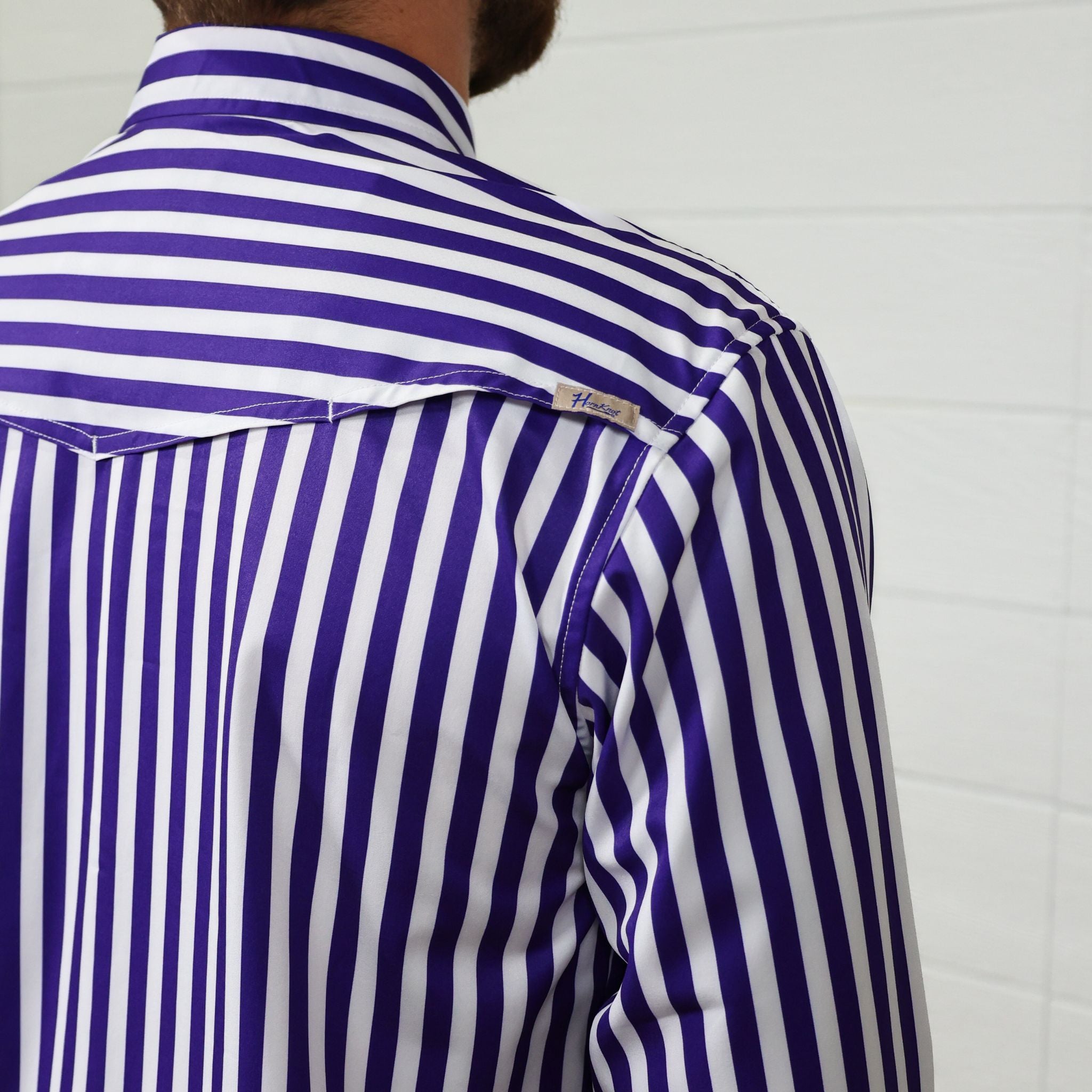 Purple and white striped shirt worn by a person against a white background, showing the vent and logo 