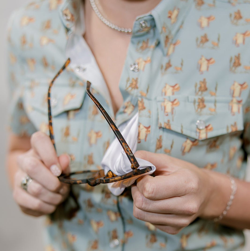 Person holding a pair of glasses with a western patterned shirt showing the built in lens cloth.