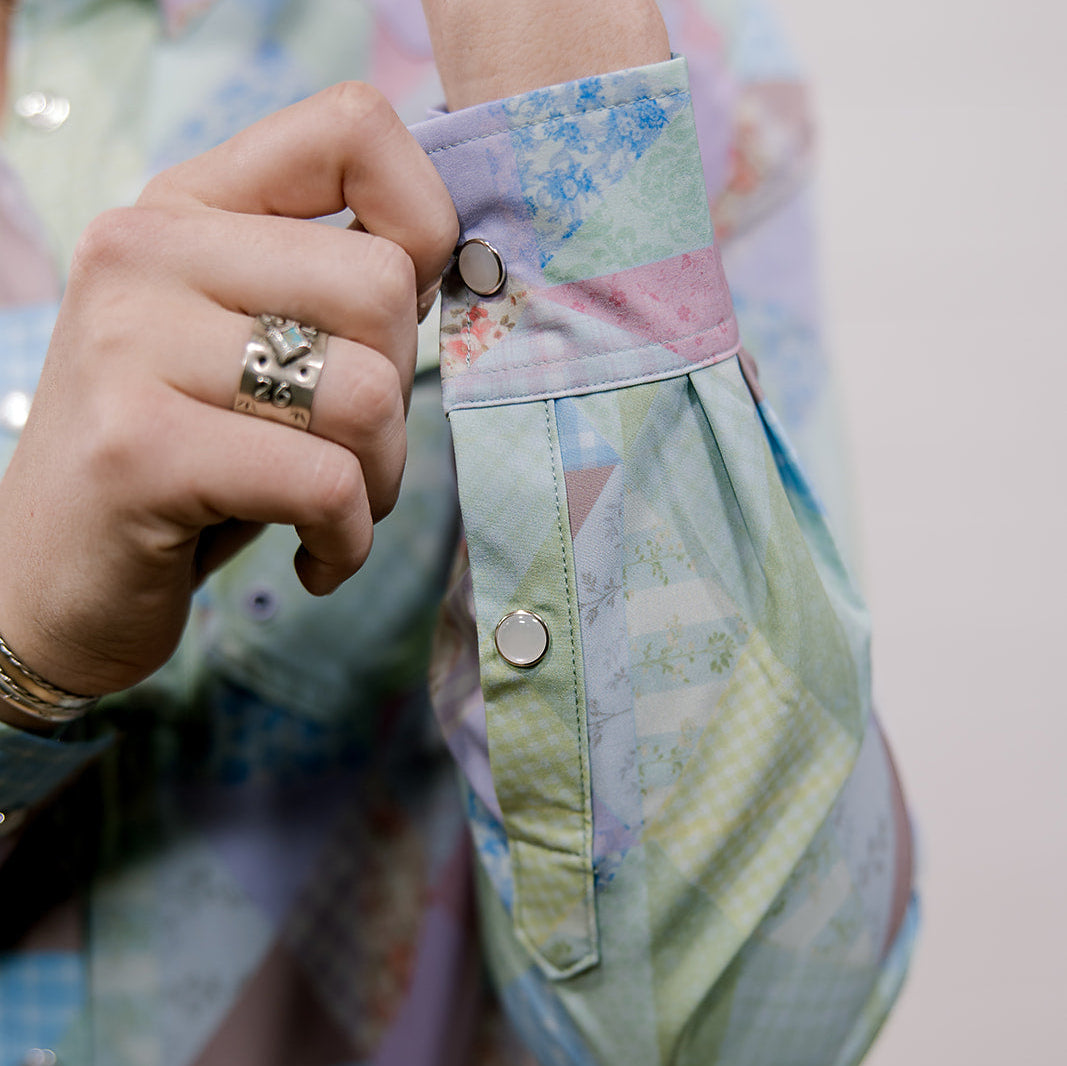 Close-up of a person buttoning a pastel-colored shirt with floral patterns.