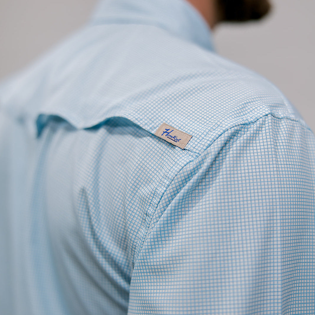 Light blue checkered shirt with a brand label on the sleeve, worn by a person. Back Facing
