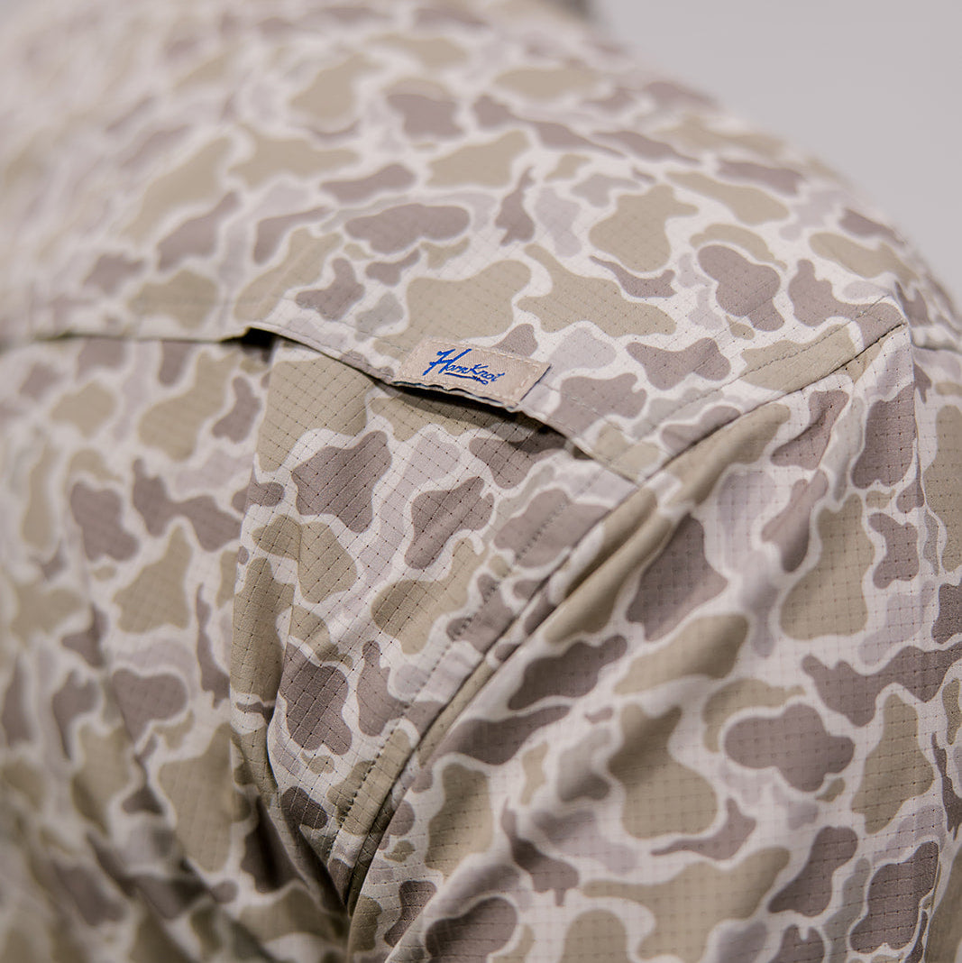 Camouflage-patterned shirt with a brand logo on a neutral background