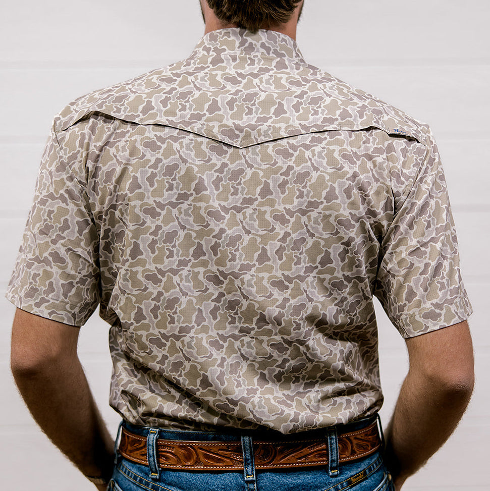 Man wearing a patterned camo shirt and jeans against a plain background. Back Facing