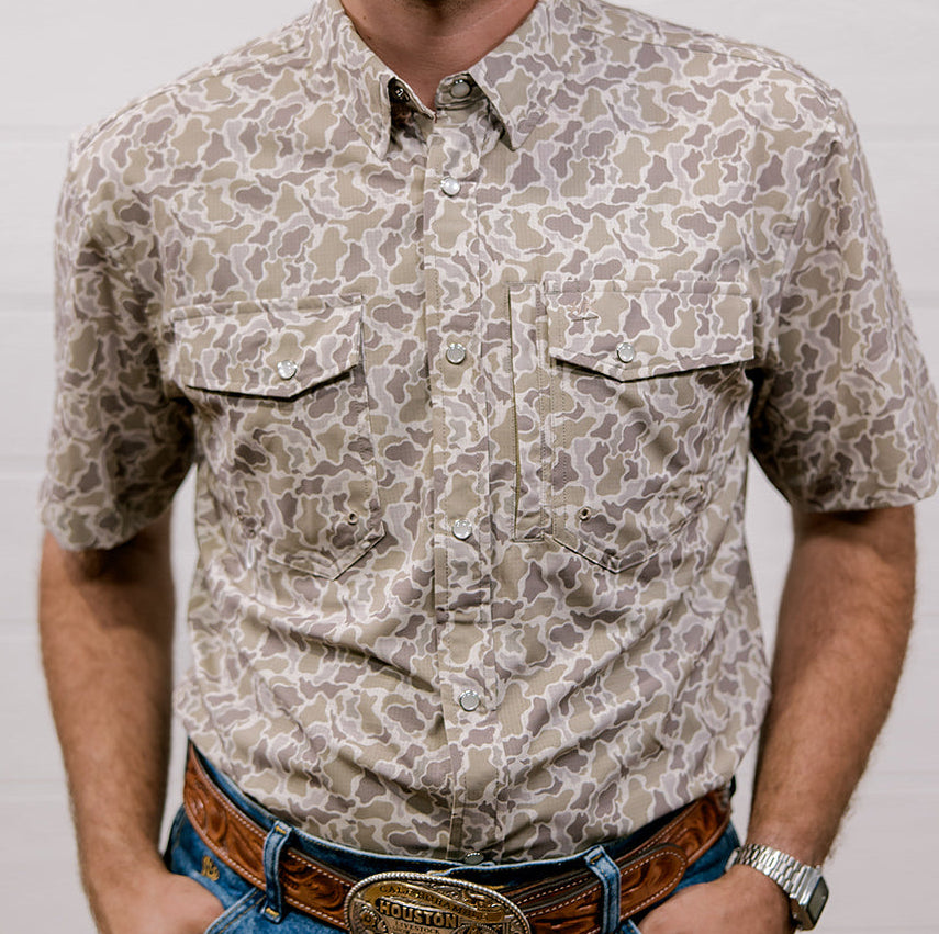 Man wearing a patterned camo shirt and jeans against a white background. Front Facing