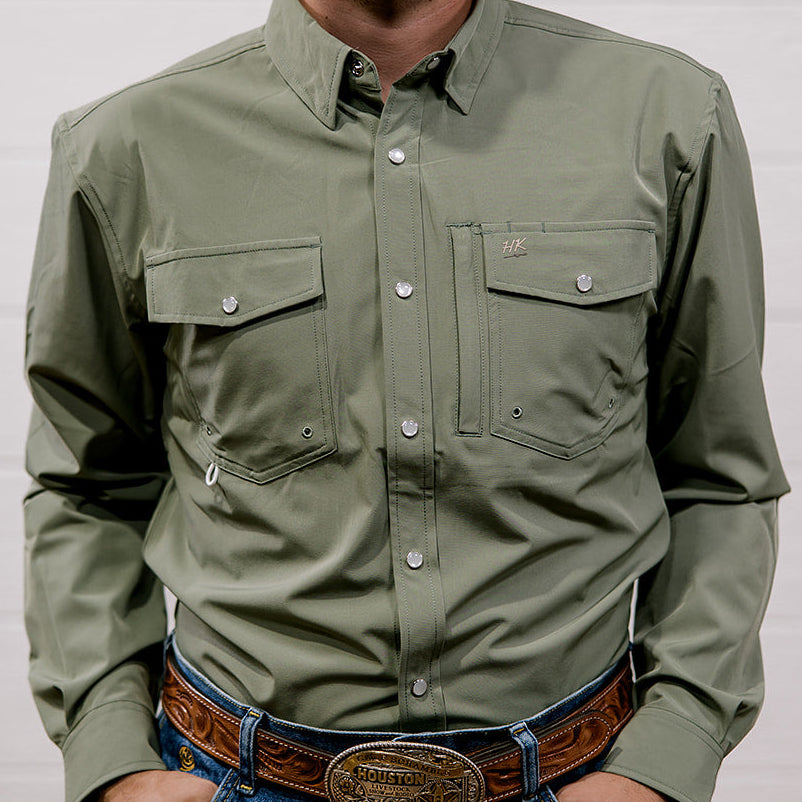 Man wearing a green shirt and blue jeans with a belt, standing against a plain background. front facing