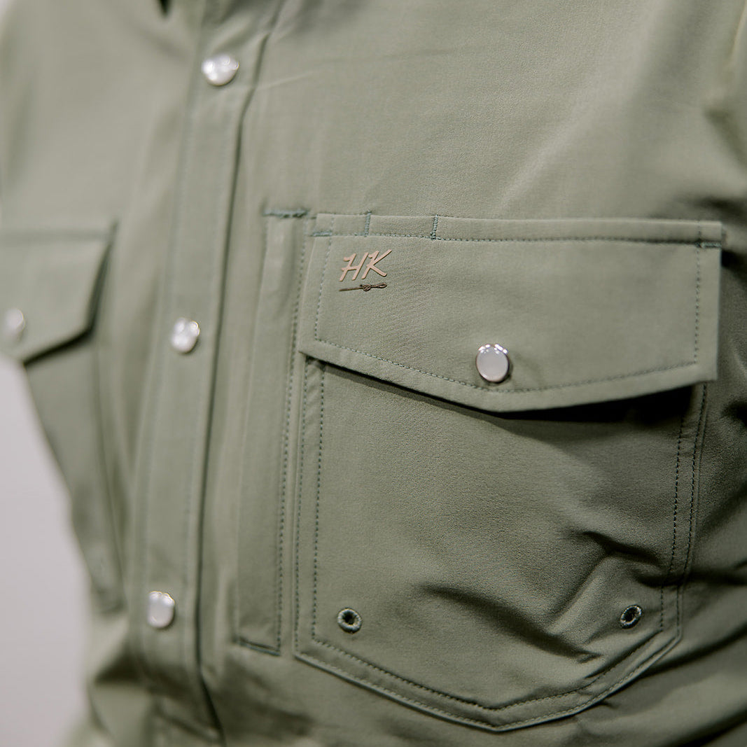 Close-up of a green shirt with a brand logo on the chest pocket. 