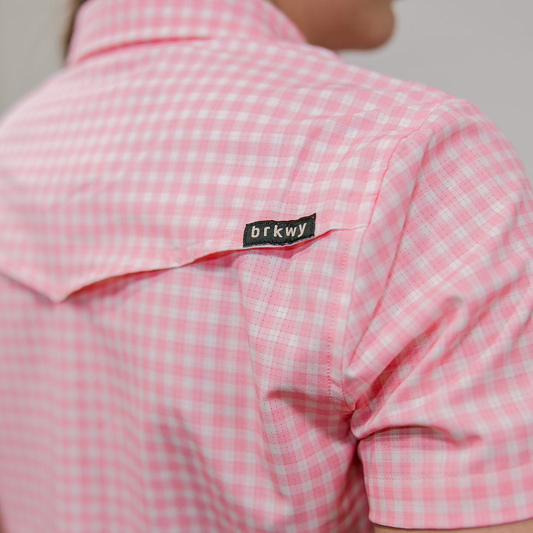 Pink checkered shirt with a brand label on the collar against a neutral background. back facing.