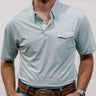 Man wearing a  blue and green patterned shirt and jeans with a belt against a plain background. front facing. 