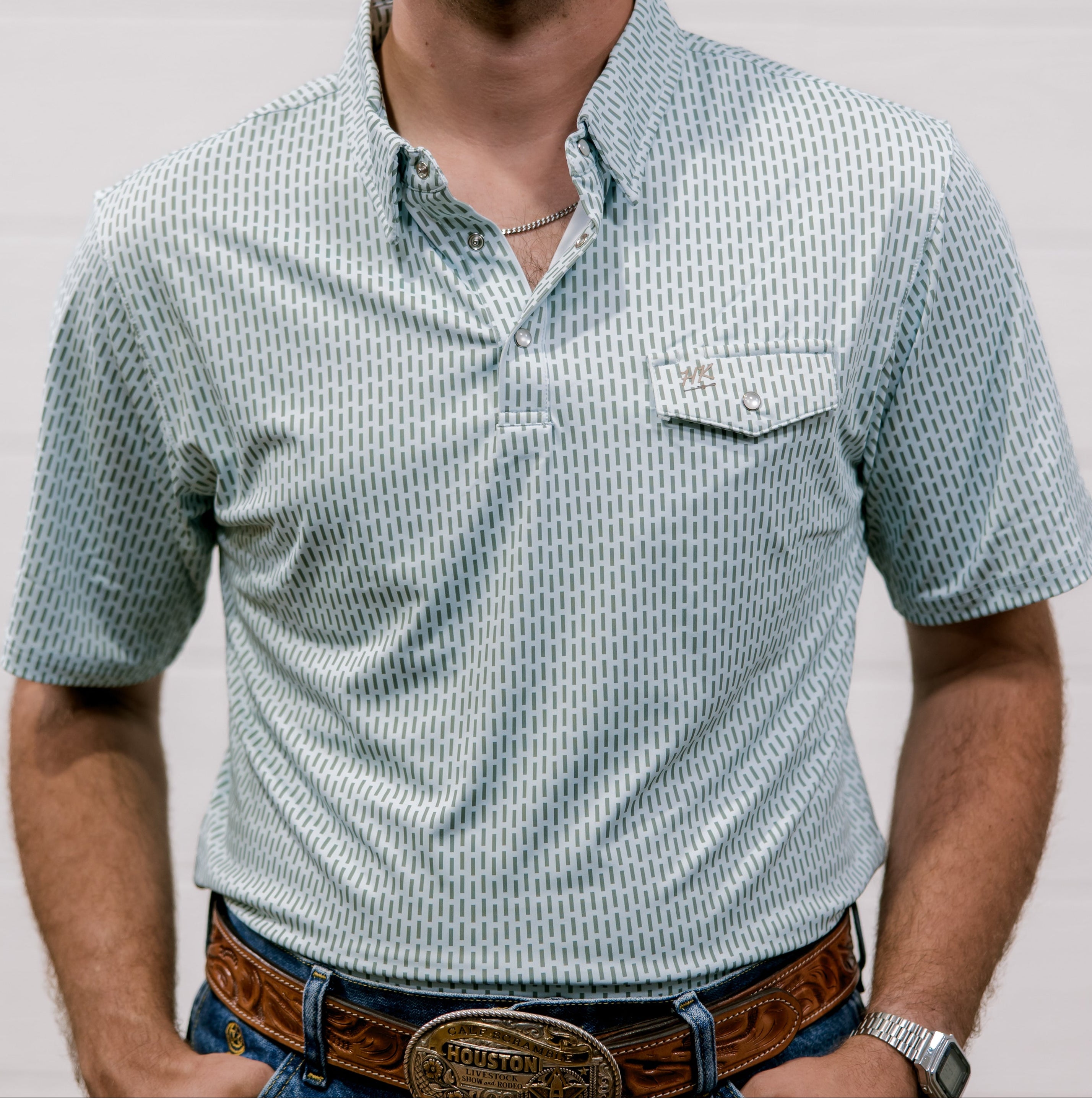 Man wearing a  blue and green patterned shirt and jeans with a belt against a plain background. front facing. 