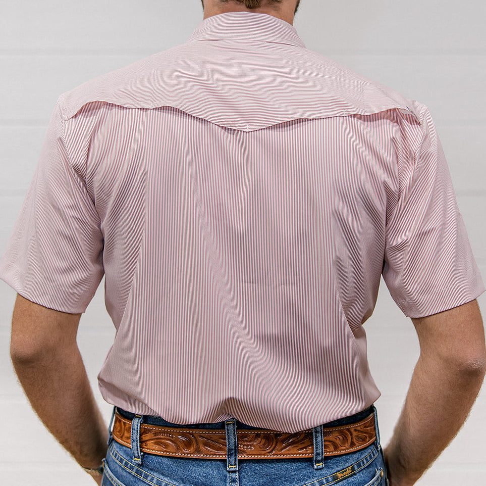 Man wearing a light pink shirt and blue jeans with a brown belt on a plain background. back facing. 