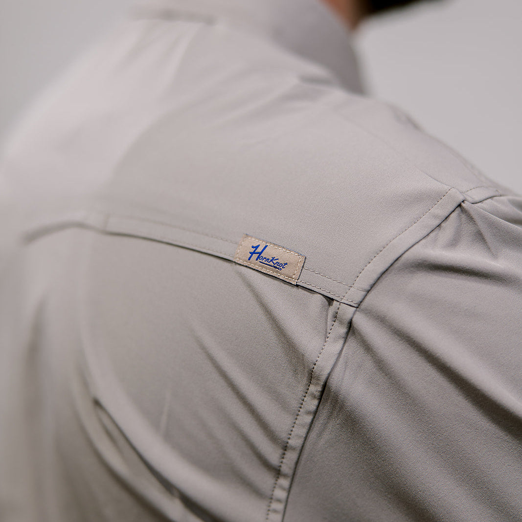 Close-up of a light grey shirt with a brand label on a neutral background. 