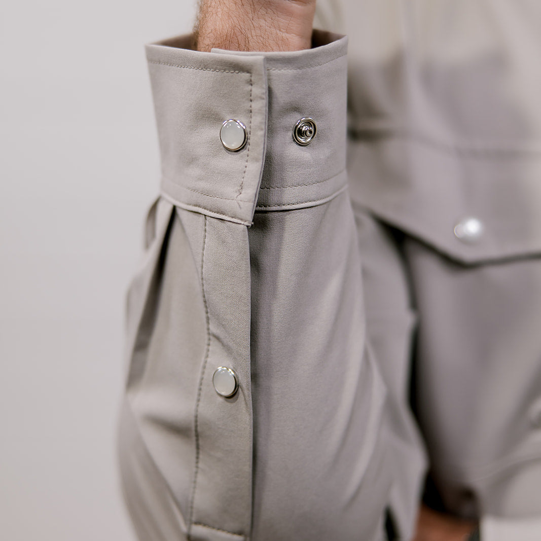 Close-up of a person wearing a light gray shirt with rolled-up sleeves on a plain background. 