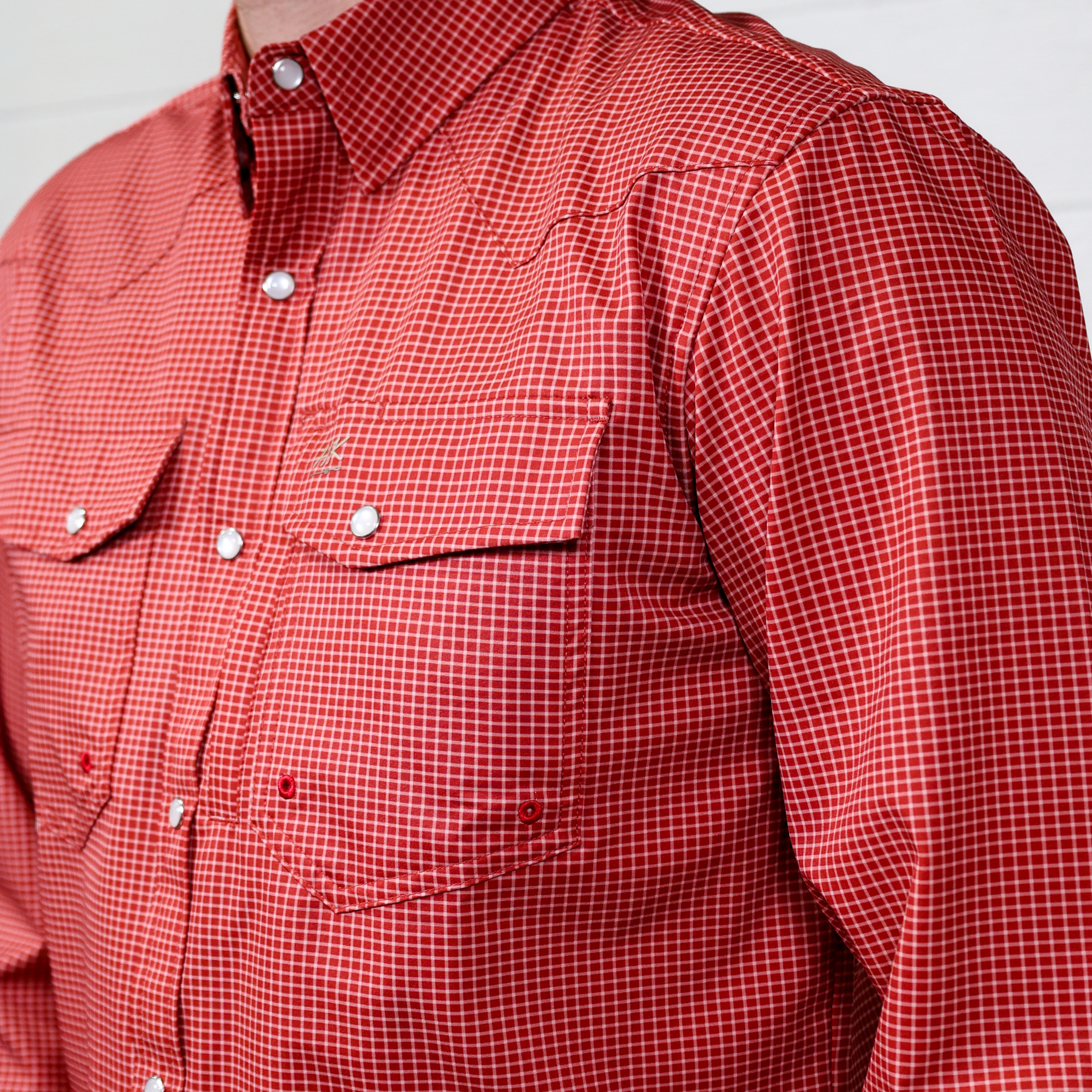 Red checkered shirt with white buttons on a plain background. side facing.