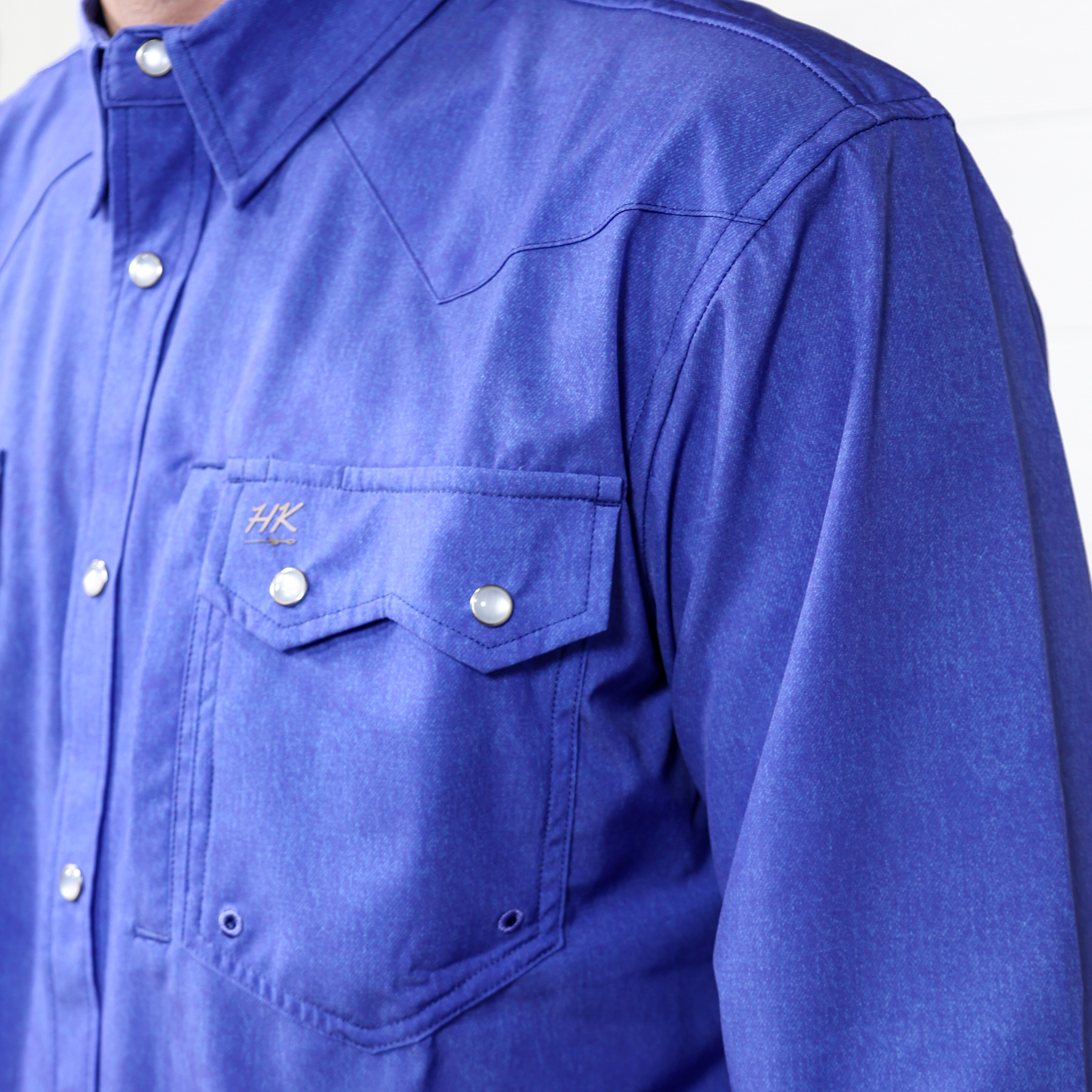 Close-up of a blue shirt with a pocket and visible brand logo on a white background. side facing 